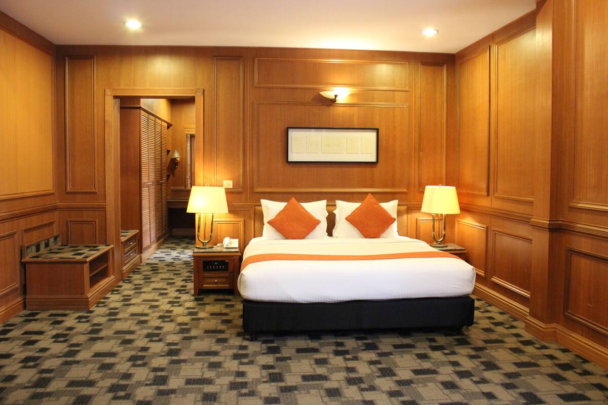 Une chambre d’hôtel avec un grand lit, deux tables de chevet avec des lampes, un tableau encadré au mur et un sol à carreaux.