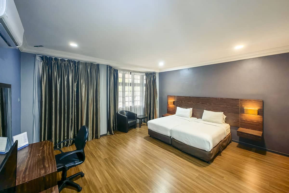 Une chambre d’hôtel avec un grand lit, un bureau avec une chaise, une fenêtre avec des rideaux et une lampe fixée au mur.