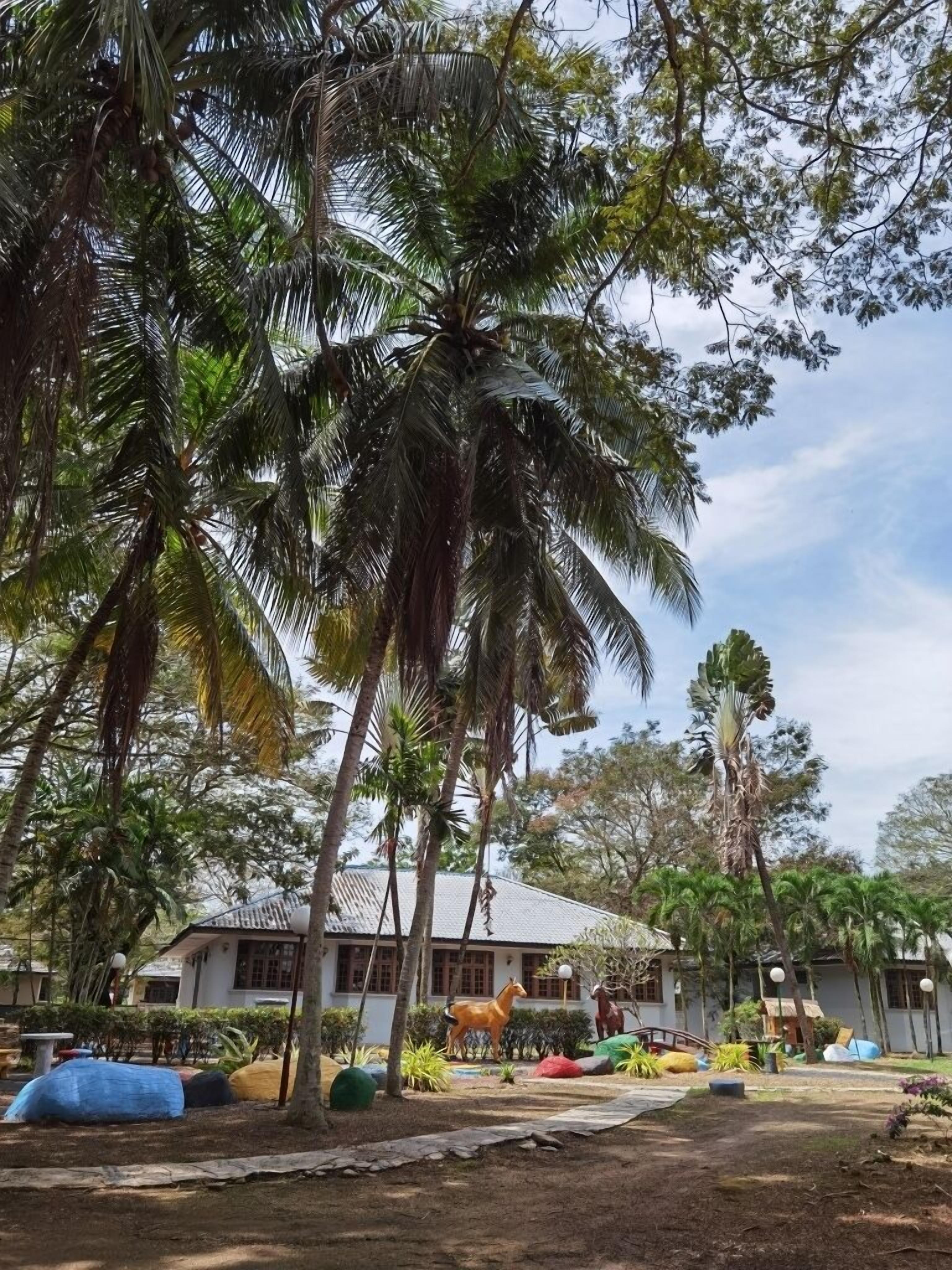 Um resort tropical com palmeiras, uma estátua de cavalo e um edifício com telhado de azulejos.