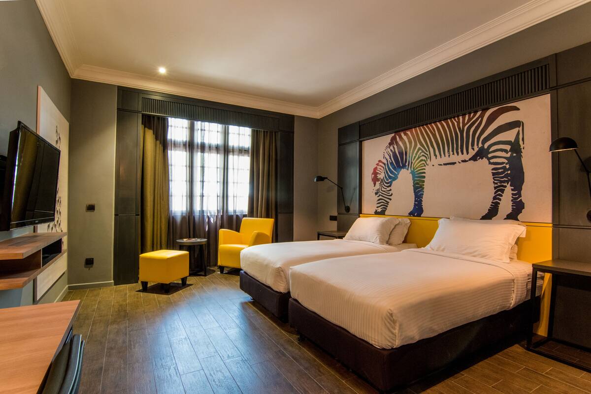 Une chambre d’hôtel avec deux lits, une télévision, un bureau, une chaise et une fresque représentant des zèbres sur le mur.