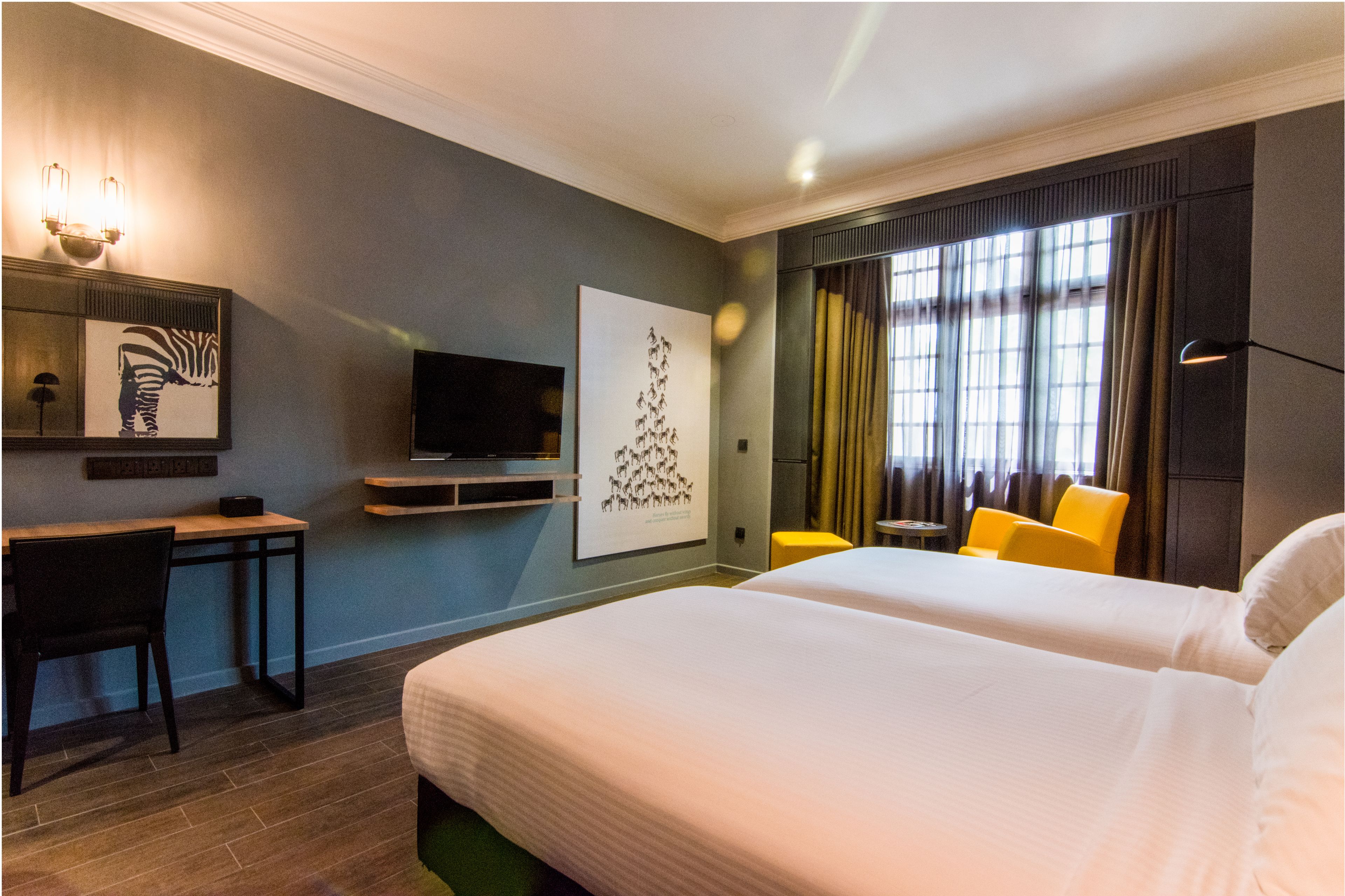 A hotel room with a bed, a desk, a chair, a television, and artwork on the wall.
