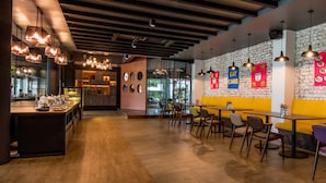 Un café moderno con mesas y sillas de madera, una pared de ladrillo con arte colorido e iluminación colgante.