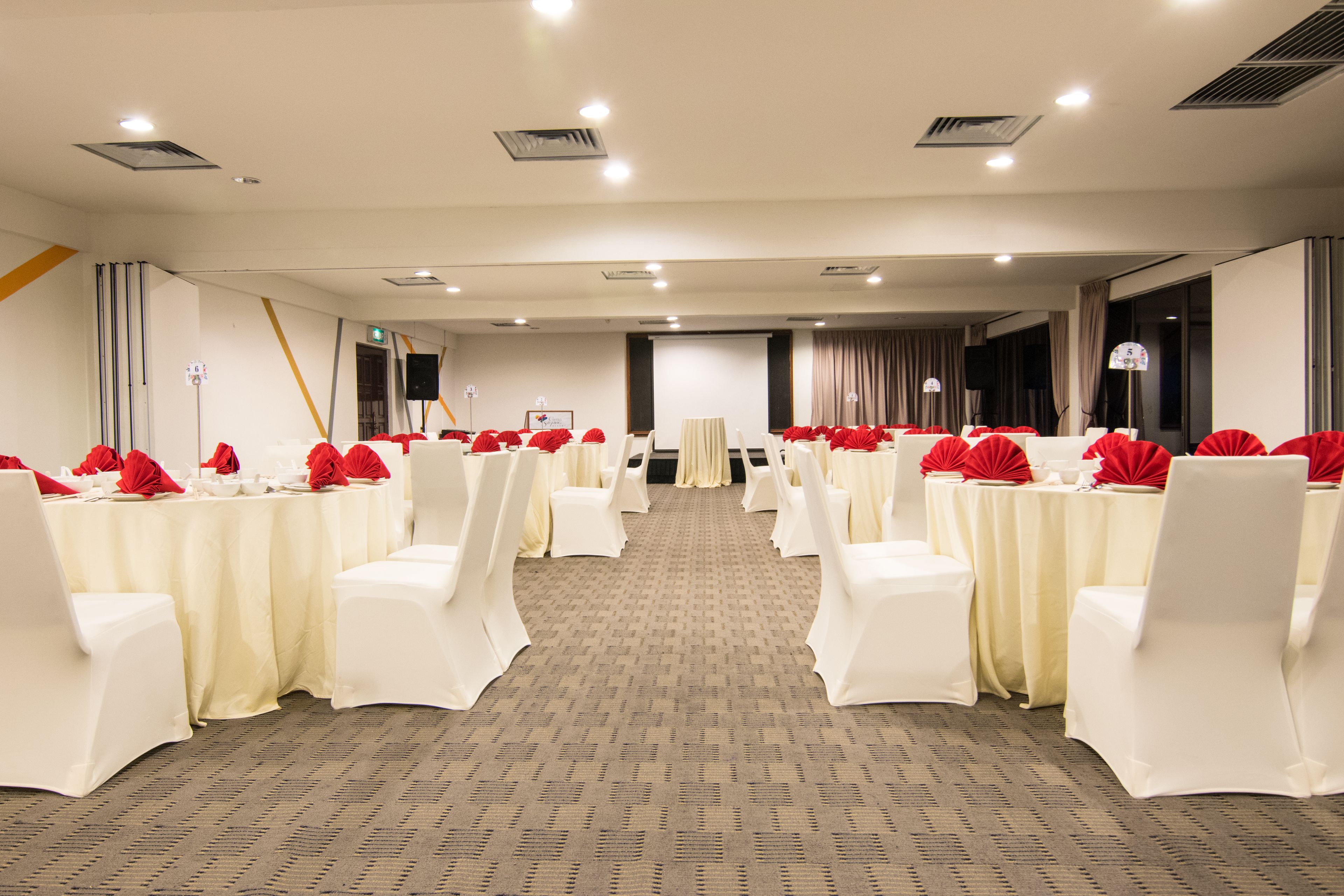 A conference room with rows of white chairs and tables, each with red decorations.