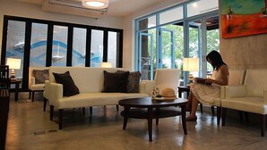 A modern lobby with a white sofa, a round table, and a large window with a view of greenery. - Apo Hotel (Krabi)