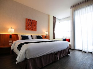 A hotel room with a large bed, two bedside lamps, a wall art piece, and a large window with curtains.