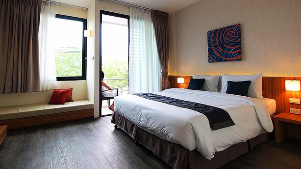 A hotel room with a large bed, a bench by the window, and a view of greenery outside. - Apo Hotel (Krabi)