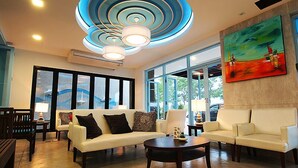 A modern lobby with a white sofa, a round coffee table, and a large window with a view of the outdoors. - Apo Hotel (Krabi)