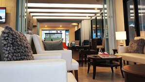 A modern hotel lobby with a seating area, a reception desk, and a large window providing a view of the outdoors. - Apo Hotel (Krabi)