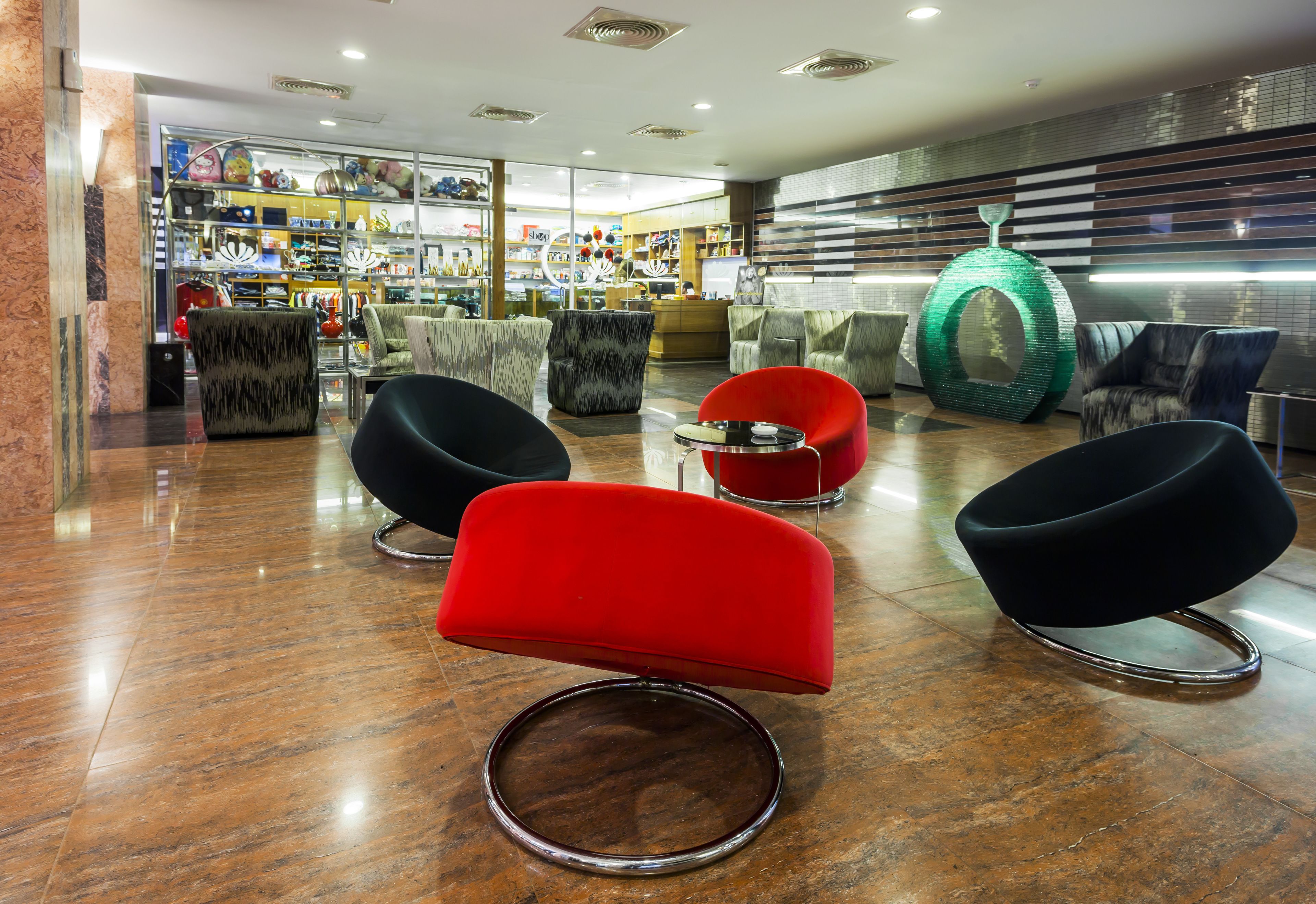 Un hall d’entrée moderne avec un sol en marbre, des fauteuils rouges et noirs, une vitrine et un élément décoratif vert.