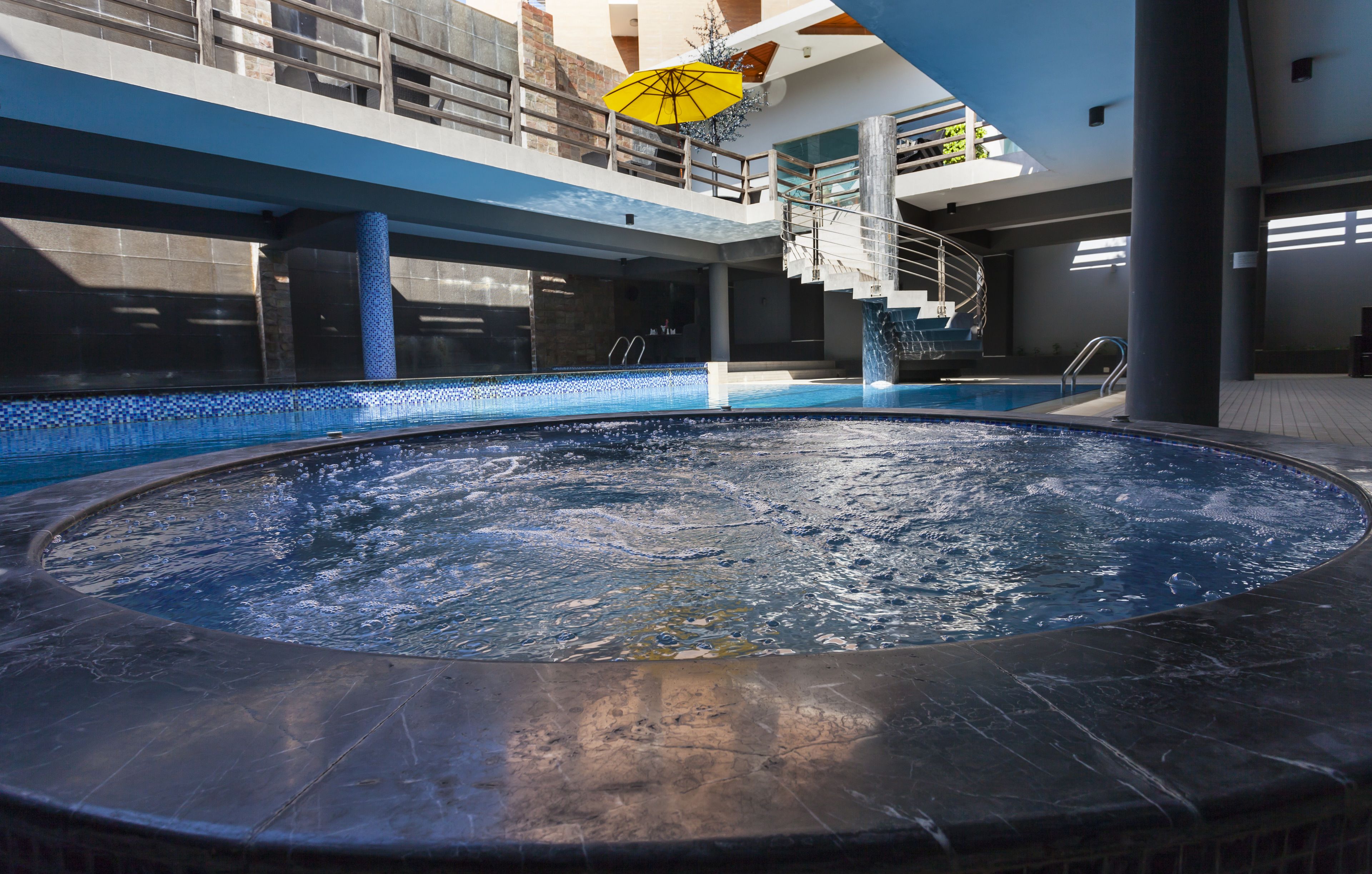 Zona de hidromasaje con piscina, escaleras y un paraguas amarillo.