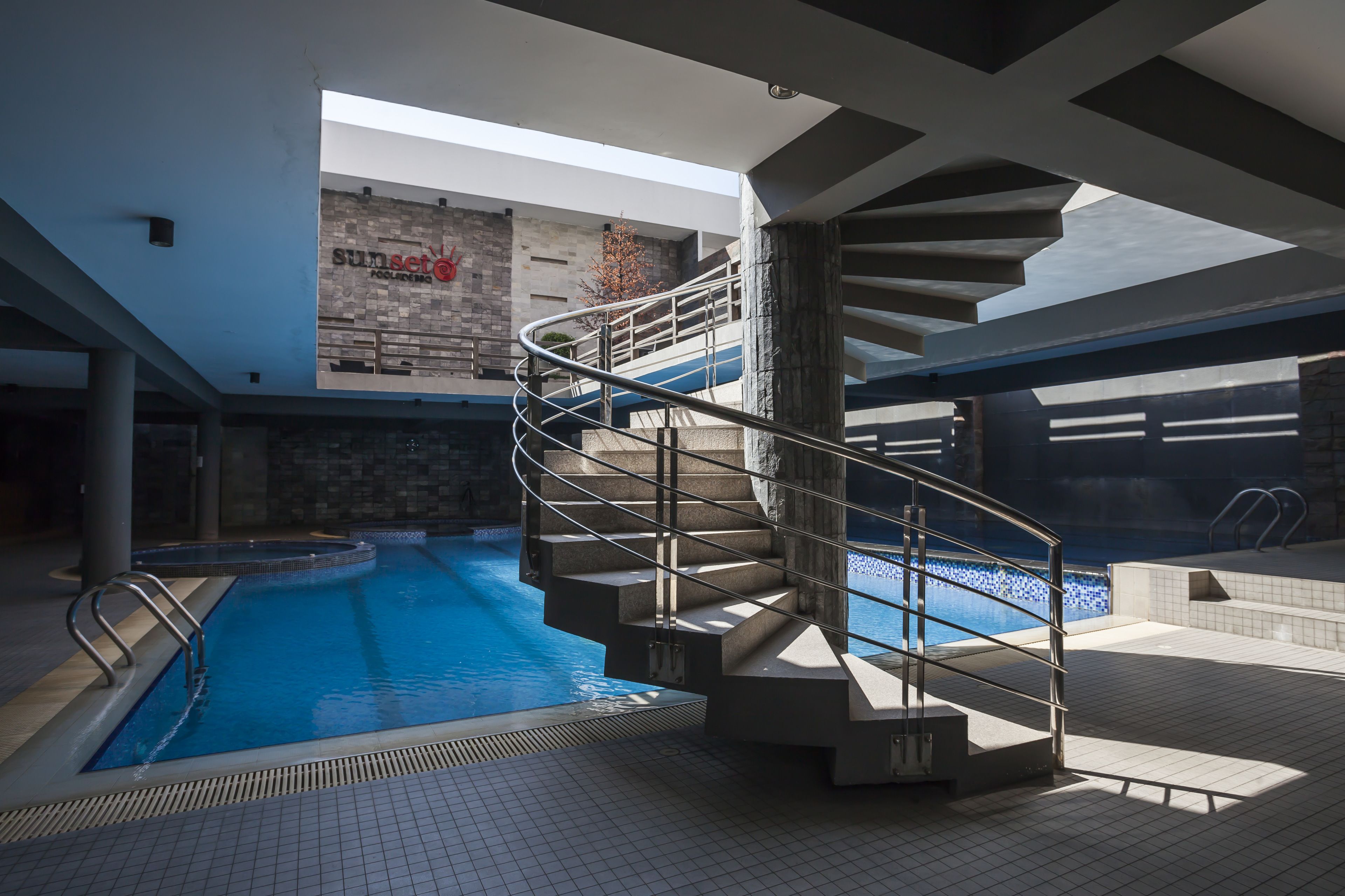 Une piscine intérieure moderne dotée d’un escalier en colimaçon menant à un espace aménagé sur le toit.