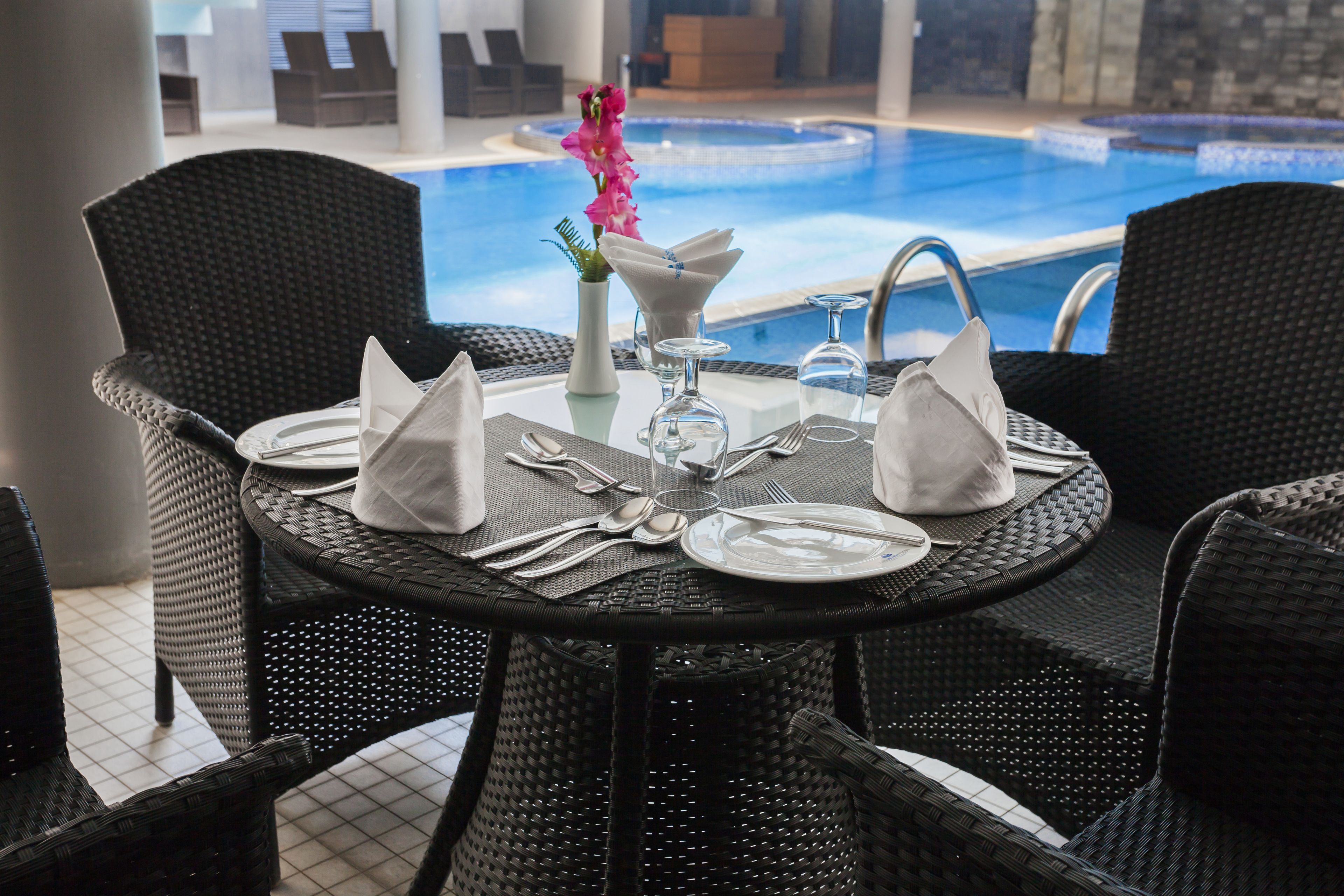 A dining table set for two with a view of a pool.