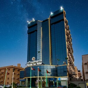 Un hotel de gran altura con fachada de vidrio moderna, señalización en árabe y banderas.
