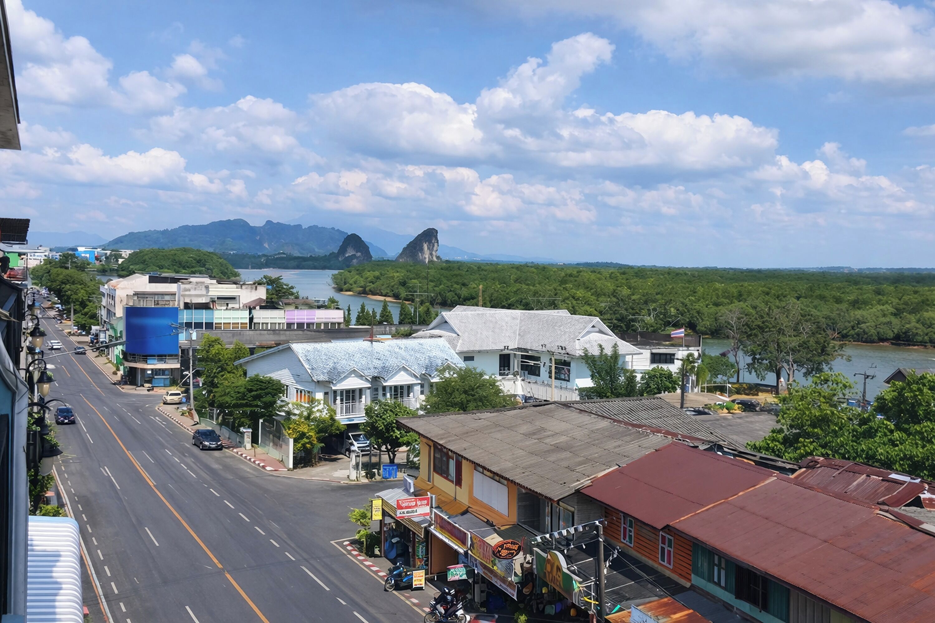 A coastal town with a road, buildings, and a view of the sea and mountains.