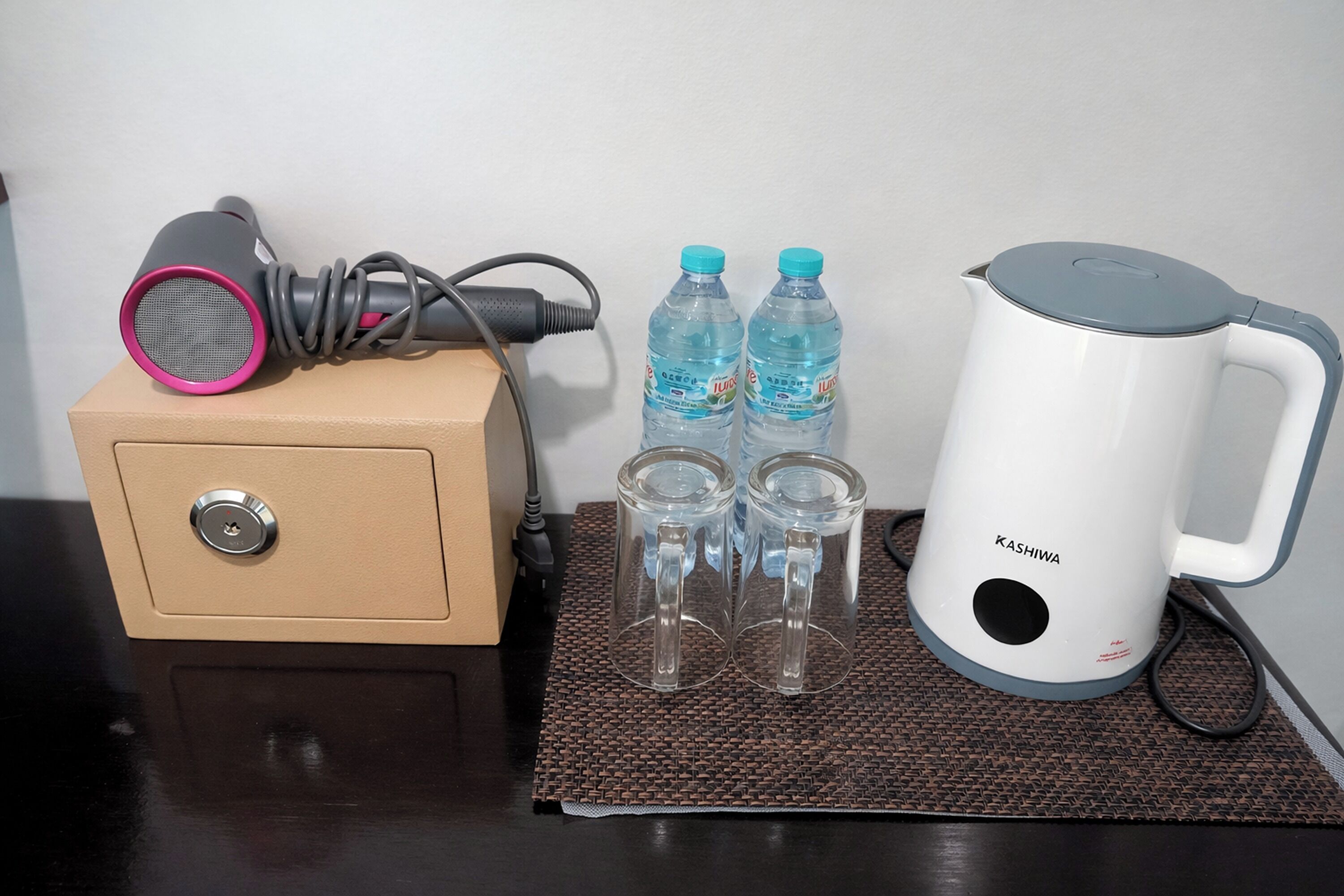 A minibar setup with a hair dryer, two water bottles, and a kettle.