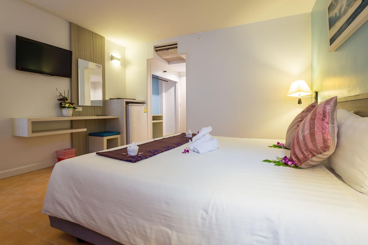 A hotel room with a bed, a TV mounted on the wall, a mirror, a small table with a plant, and a nightstand with a lamp.