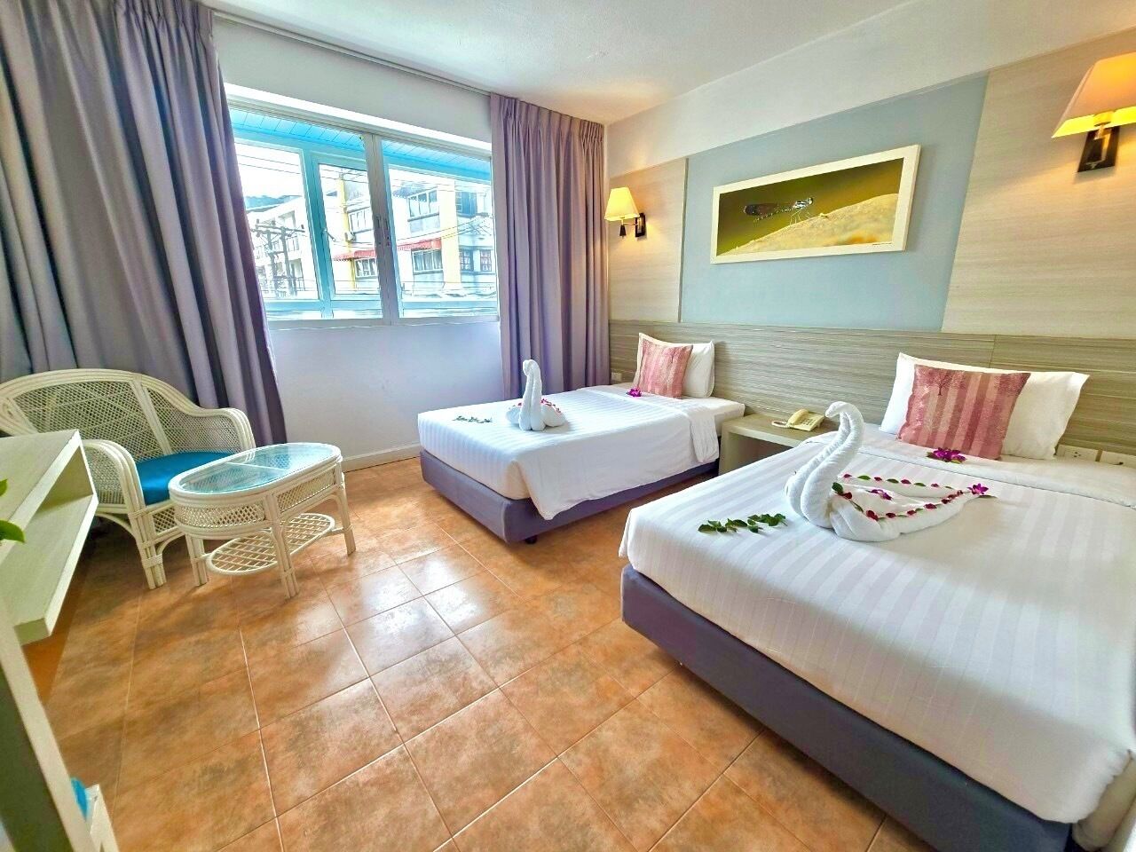 A hotel room with two beds, a small table, a chair, and a window with curtains.