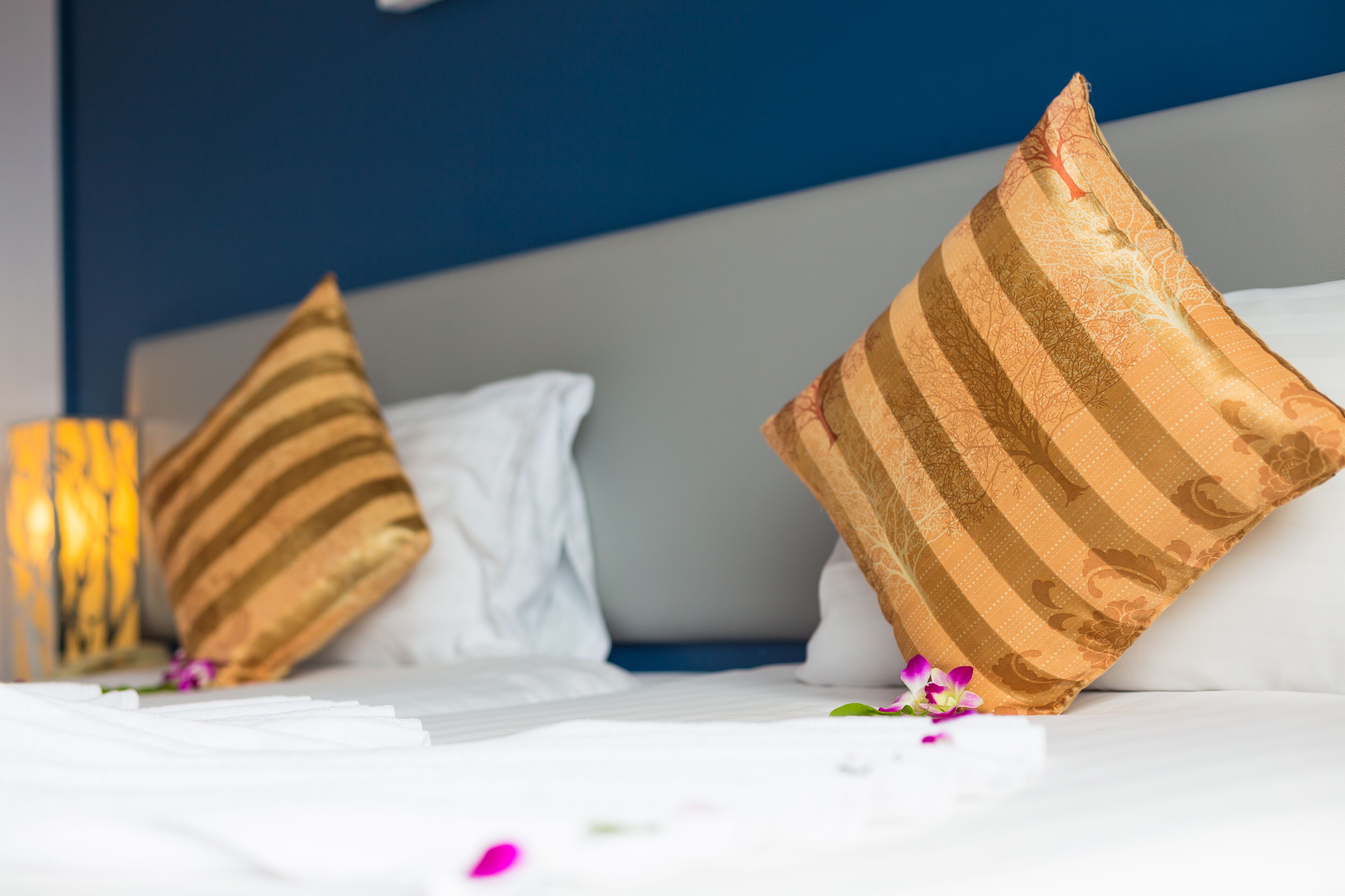 A neatly made bed with striped pillows and a white pillow, a decorative vase, and scattered flowers.