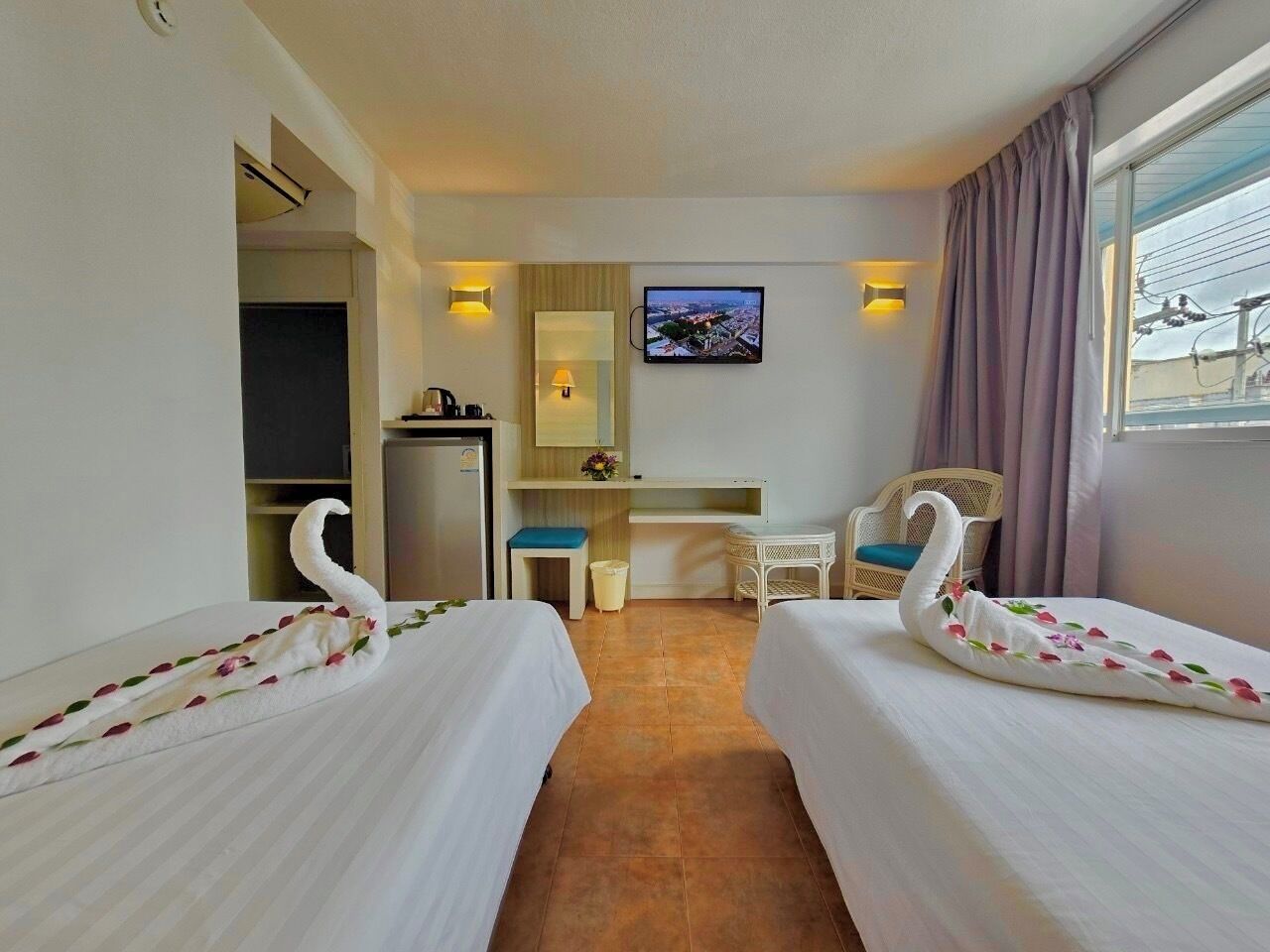 A hotel room with two beds, a desk, a chair, a television, and a window with curtains.