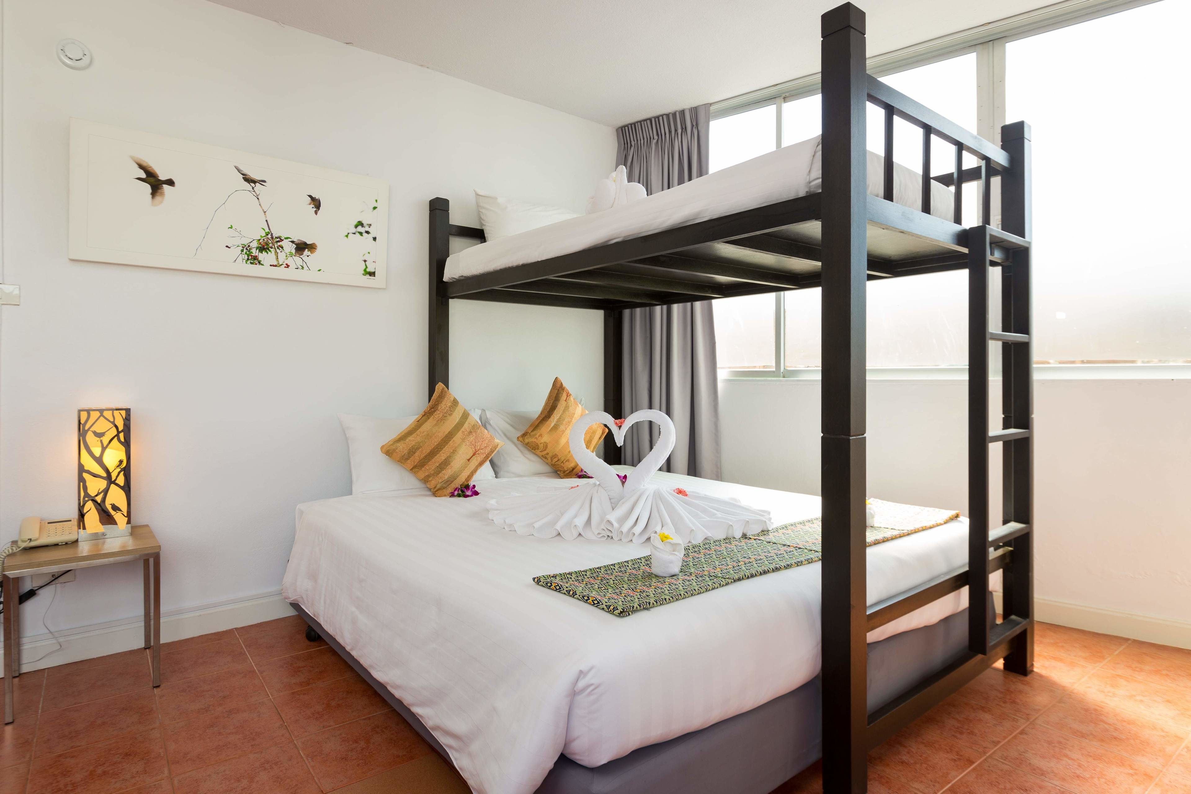 A bunk bed room with a white bedspread, pillows, a decorative swan towel, a small table with a lamp, and a wall art piece.