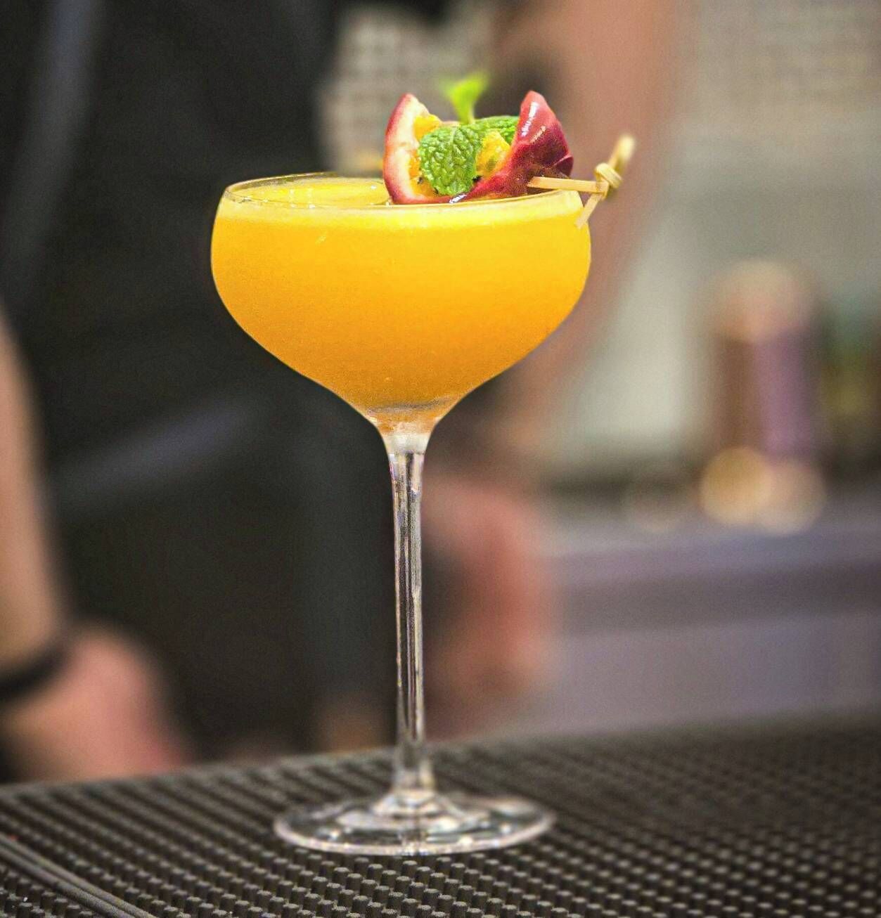 A cocktail in a martini glass with a fruit garnish on a bar counter.