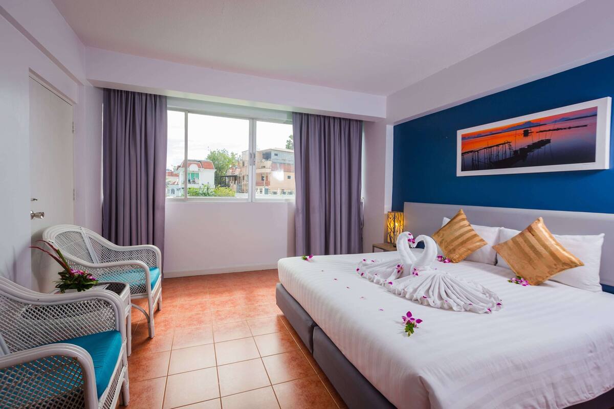A hotel room with a bed, two chairs, a window, and a painting on the wall.