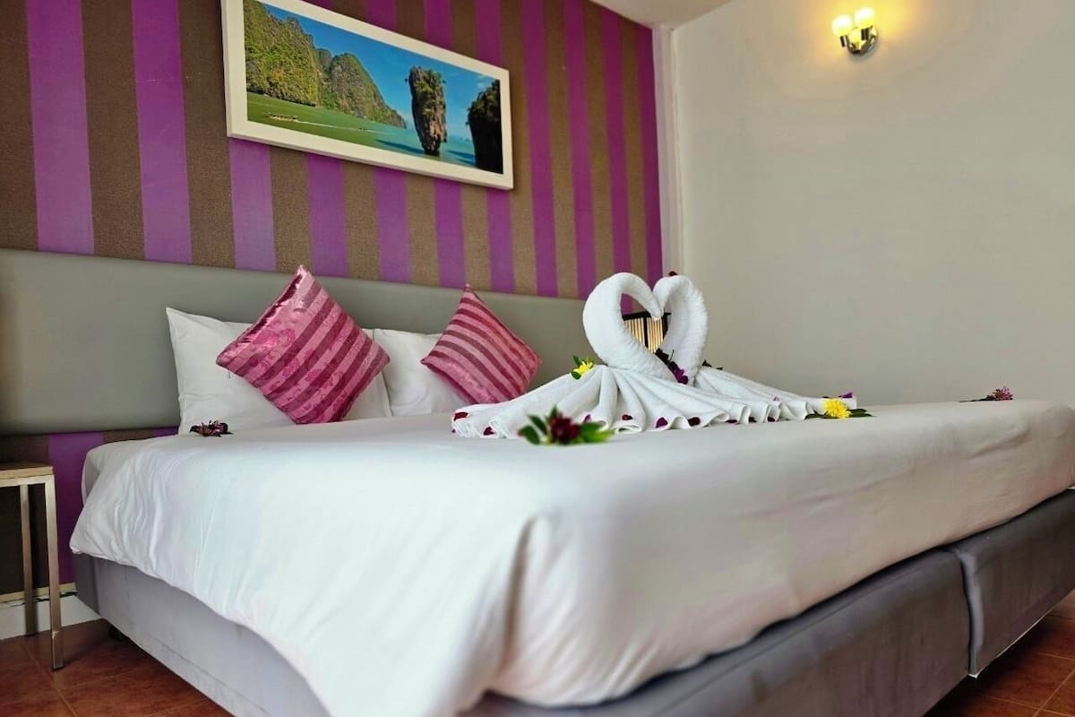 A neatly made bed with a white comforter, pink striped pillows, and a heart-shaped towel arrangement.