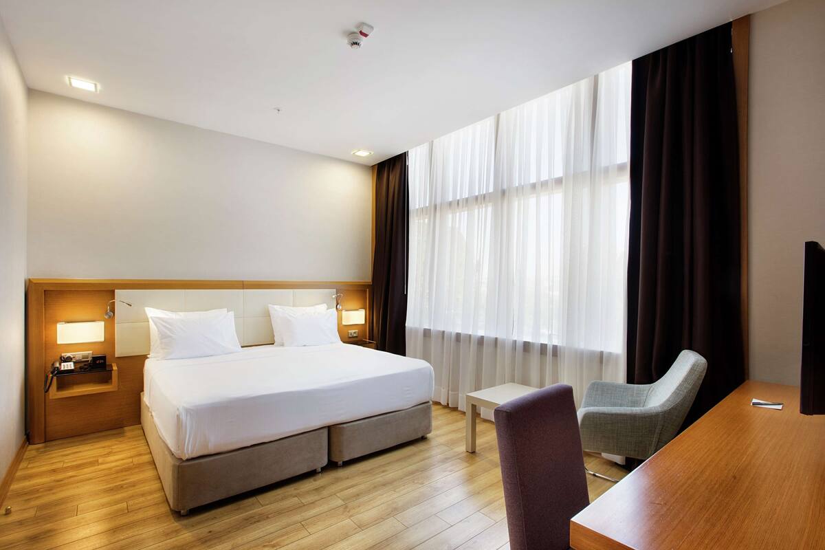 A hotel room with a large bed, a desk, a chair, and a TV.