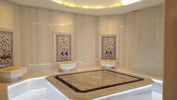 Relax in a spacious bathroom with a large bathtub, two pedestal sinks, and intricate tile work.