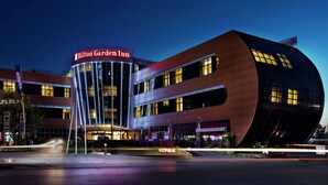 A modern building with a curved facade, a prominent sign for Hilton Garden Inn, and a nearby steakhouse.