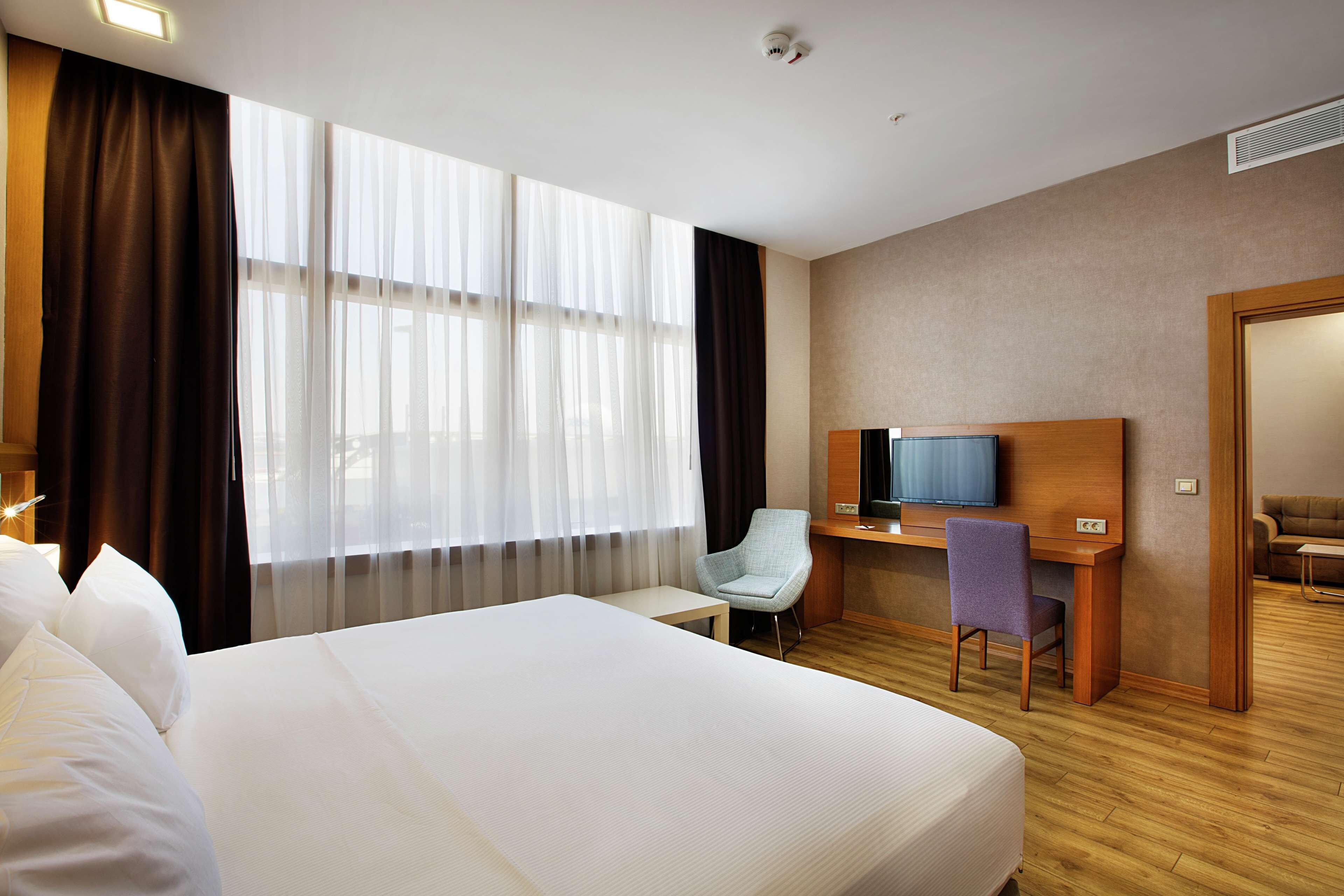 A hotel room with a large bed, a desk with a chair, a television, and a sofa.