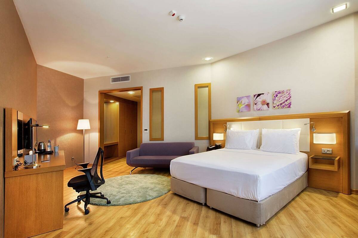 A hotel room with a bed, a desk, a chair, a sofa, and a TV.