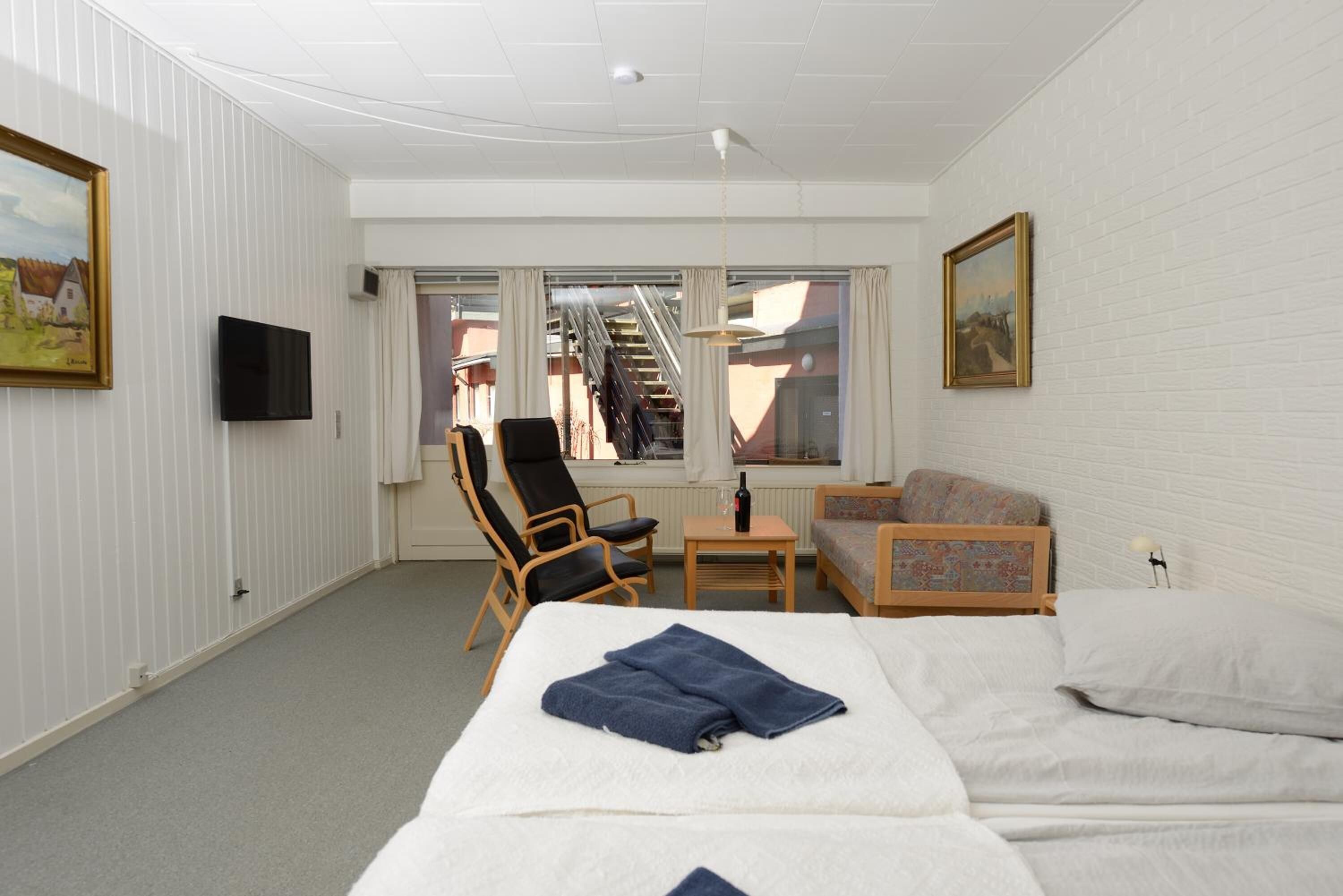 Et hotelværelse med seng, stol, sofa, fjernsyn og et vindue med udsigt til bygninger.