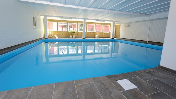 Una piscina interna con acqua cristallina, pareti in legno e pavimento piastrellato.