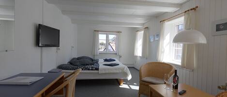 Ein Zimmer mit einem Bett, einem Schreibtisch, einem Stuhl, einem Fernseher und einem Fenster mit Vorhängen.
