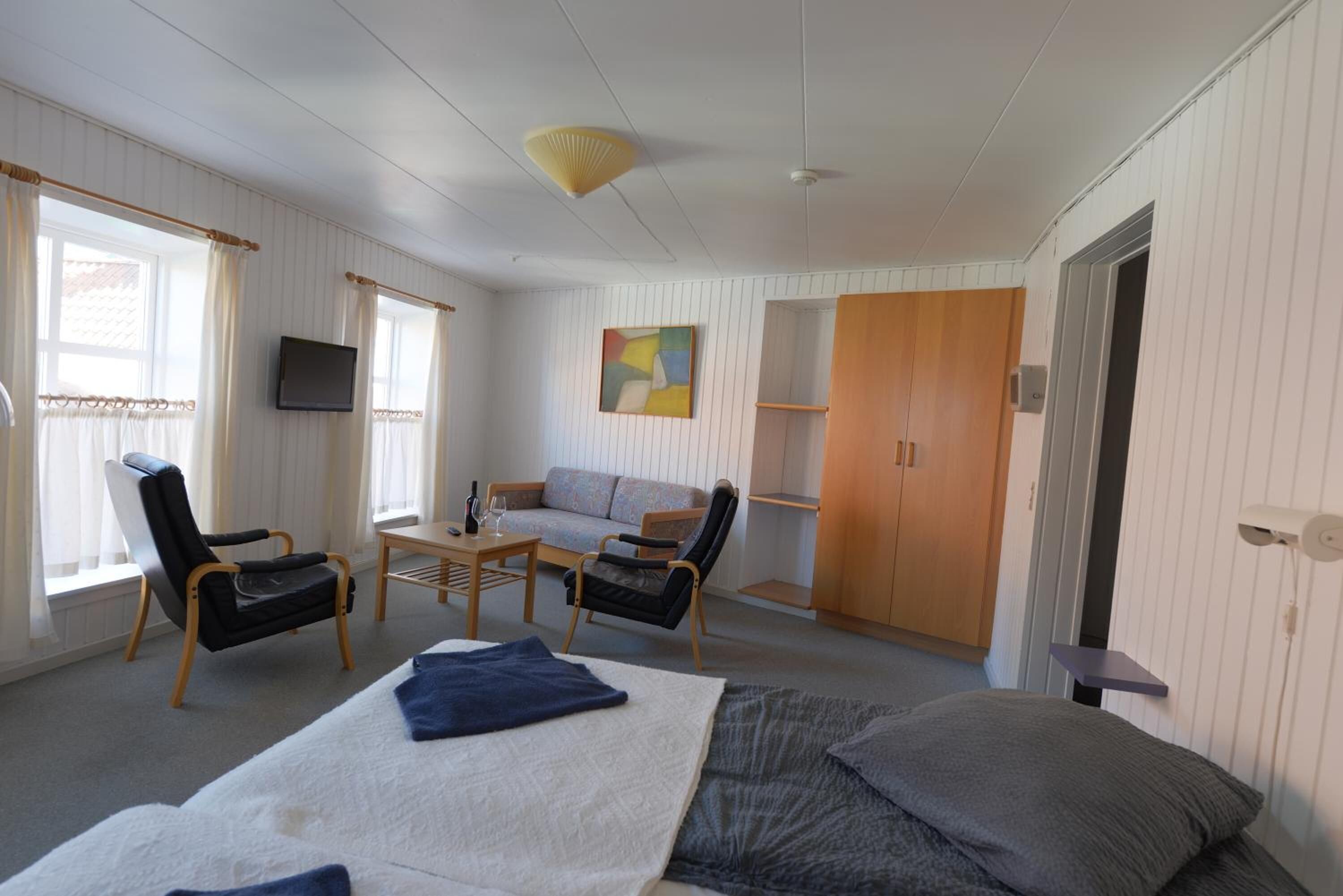 Quarto com uma cama, duas poltronas, um sofá, uma televisão e um quadro.