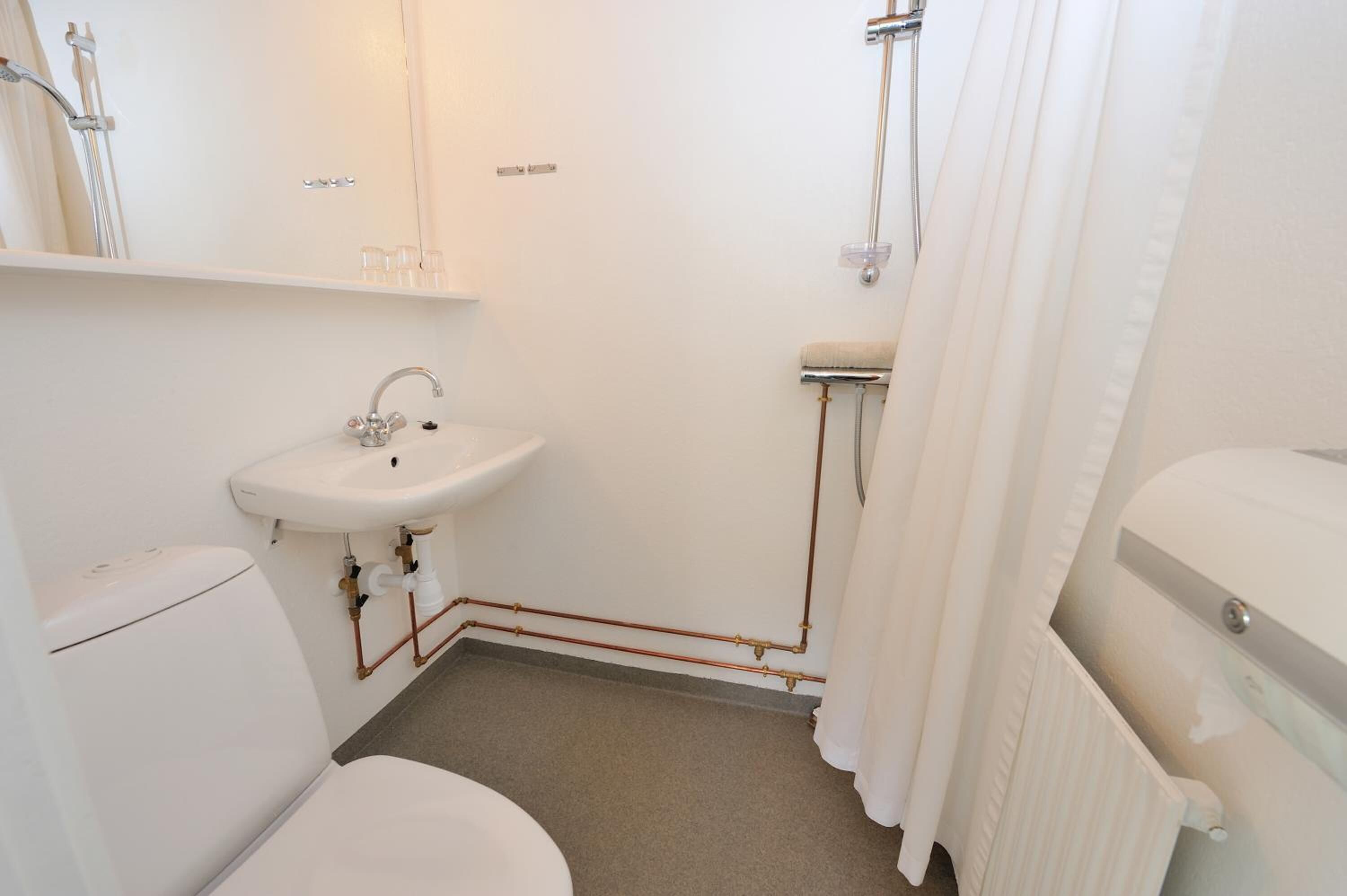 Pieni, valkoinen kylpyhuone, jossa on wc, pesuallas ja suihku.