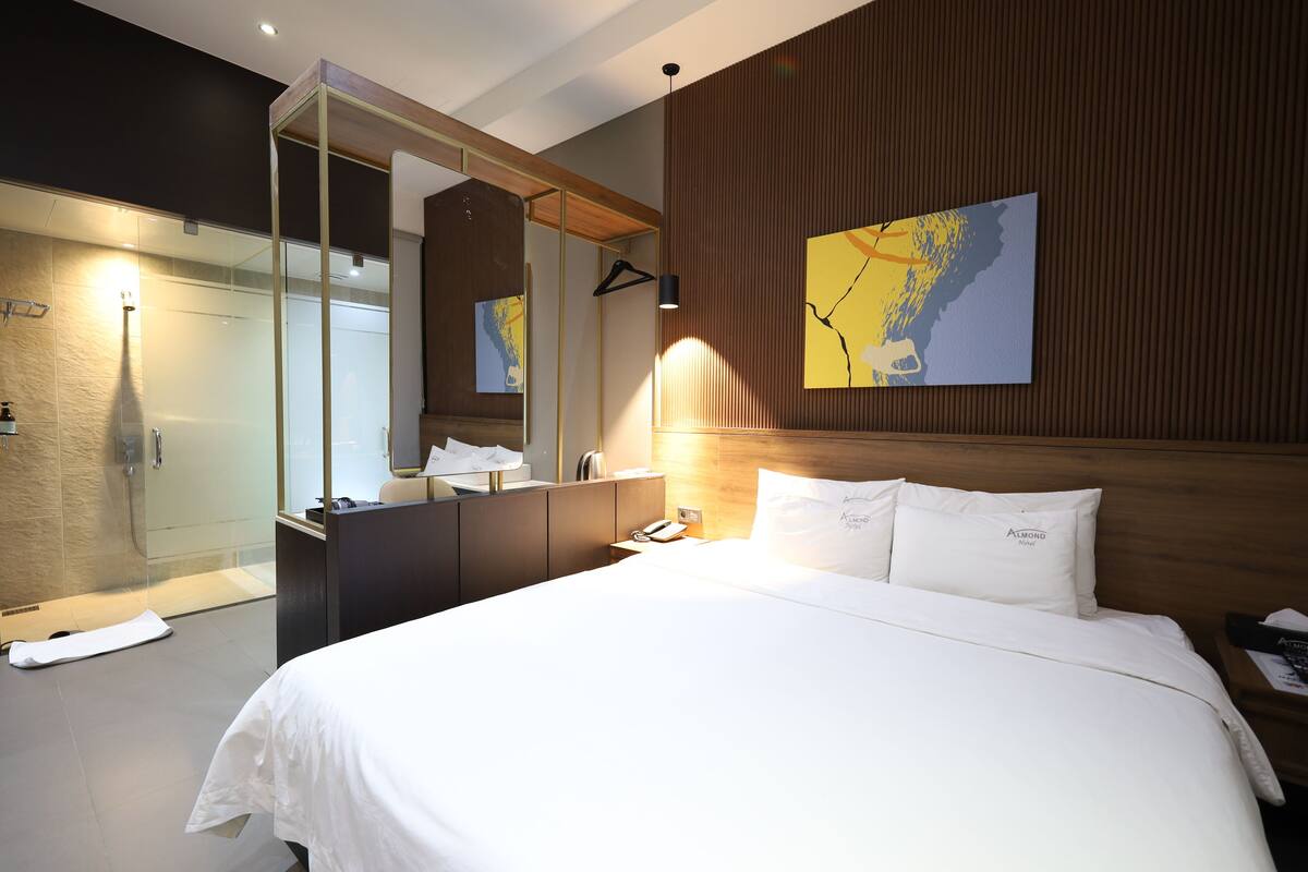 A hotel room with a large bed, a wooden headboard, a mirror, a shower area, and a map on the wall.