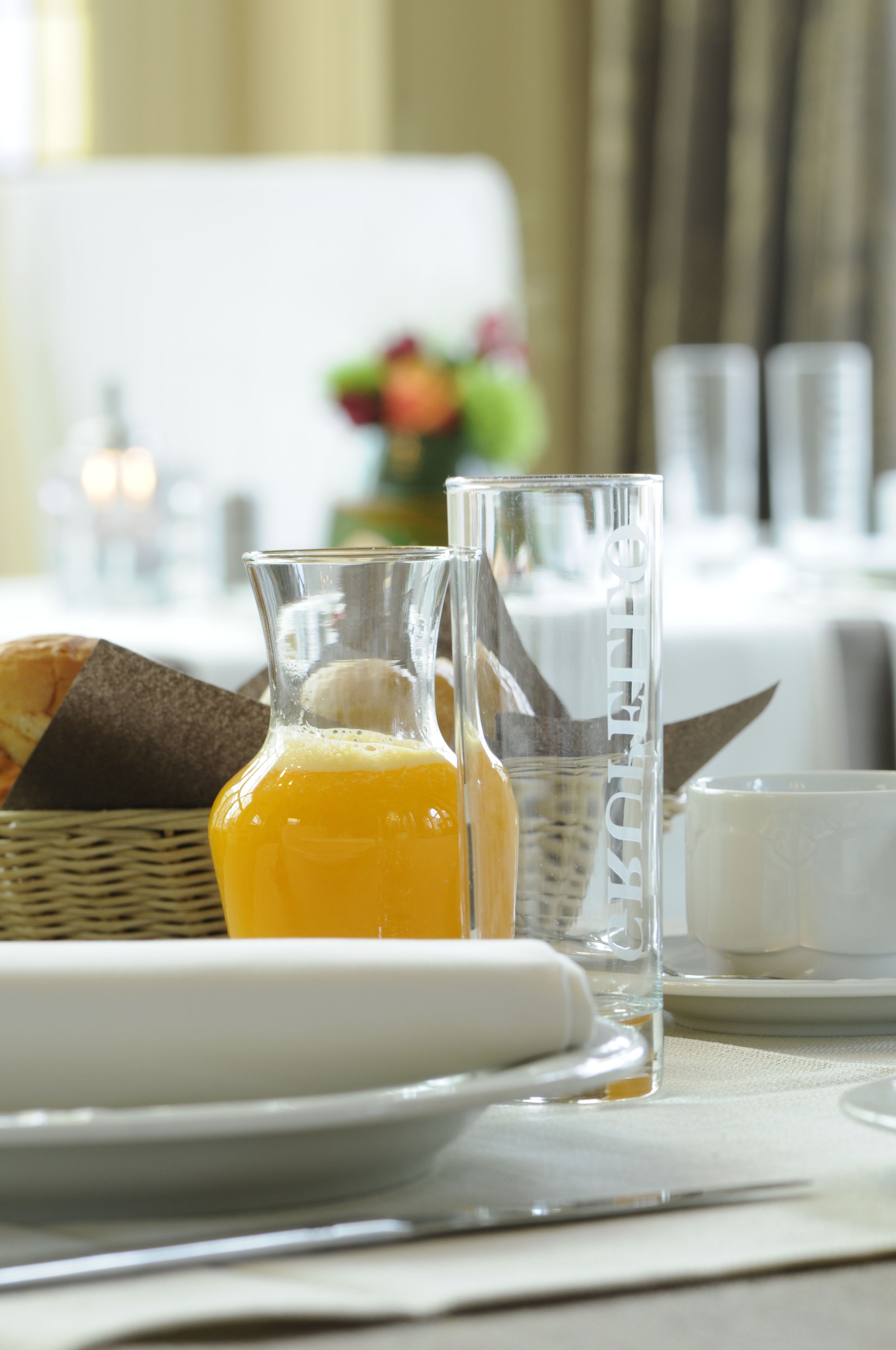 Une table mise pour le petit-déjeuner, avec une carafe en verre remplie de jus d’orange, un verre d’eau et une assiette de pain.