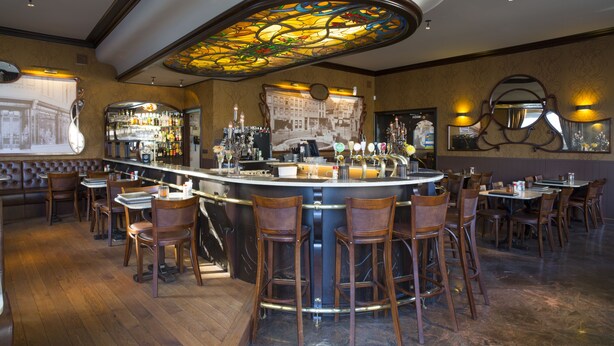 Una zona de bar con una barra curva, varios taburetes y un amplio techo de vitrales.