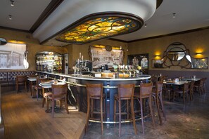 A bar area with a curved counter, multiple stools, and a large stained glass ceiling. - Hotel Grupello (Geraardsbergen)
