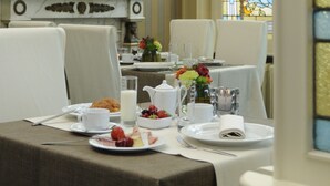 Mesa de desayuno lista, con un centro de mesa floral, mantel blanco y vistas a un ventanal de vitral.