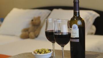 A bottle of wine, two glasses of red wine, and a bowl of olives on a table in a hotel room.
