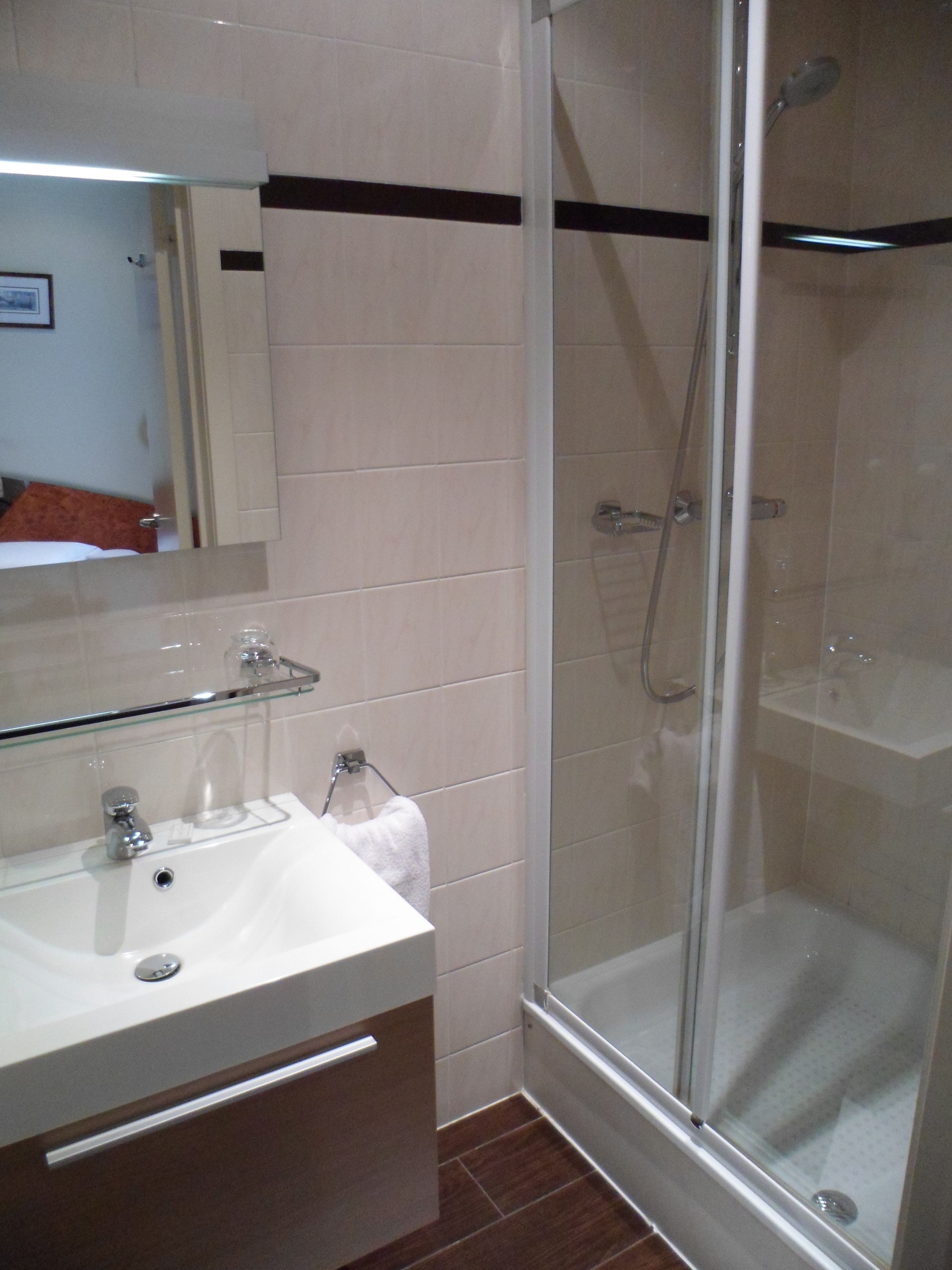 Un baño con cabina de ducha de vidrio, un lavamanos blanco y un espejo sobre él.