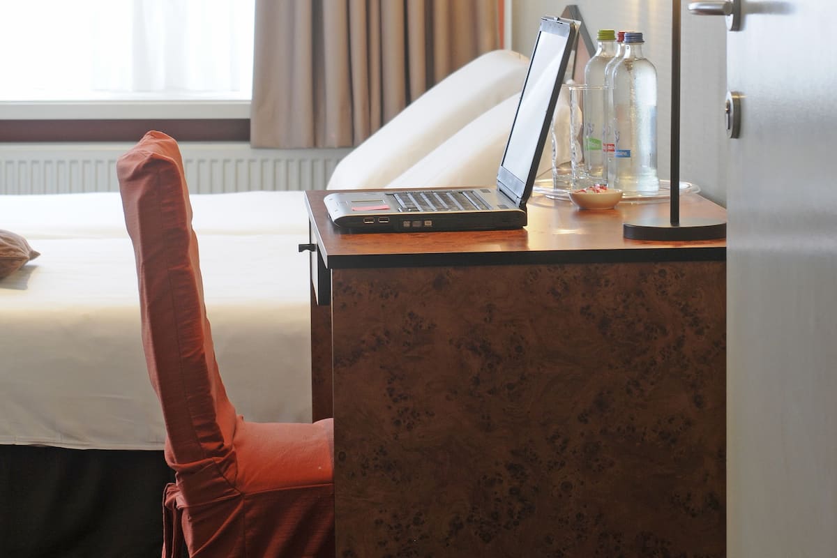 A hotel room with a bed, a desk with a laptop, a lamp, and a window with curtains.