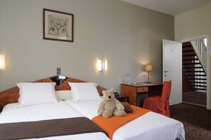 A hotel room with a bed, a desk, a chair, a teddy bear, and a staircase.
