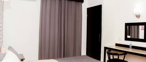 A hotel room with a bed, a desk with a chair, a mirror, and a window with curtains.