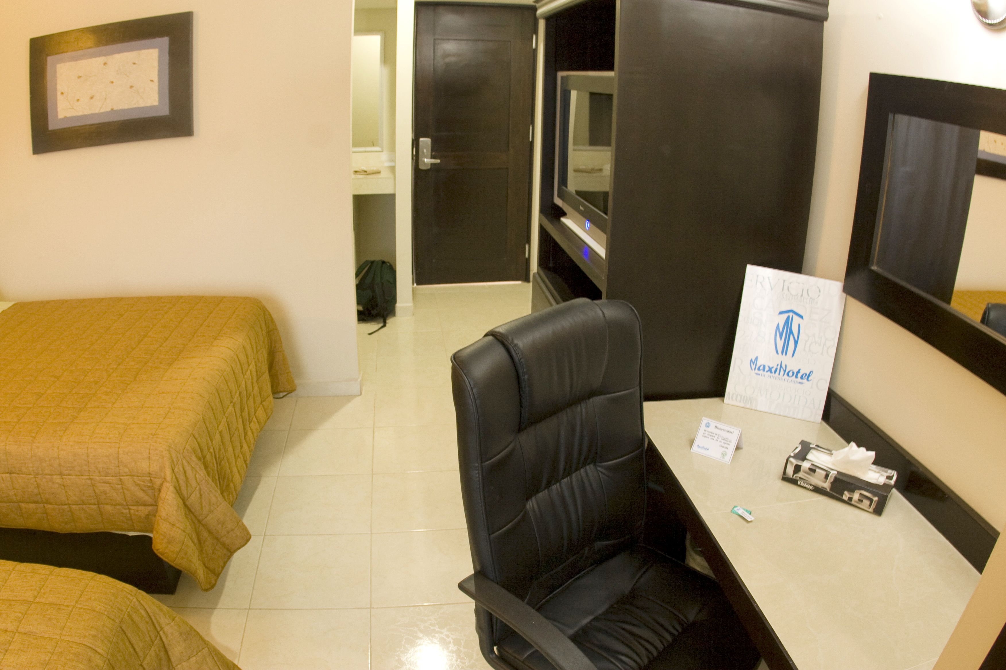 Habitación de hotel con cama, escritorio, silla, televisor y un cartel de Maxihotel.