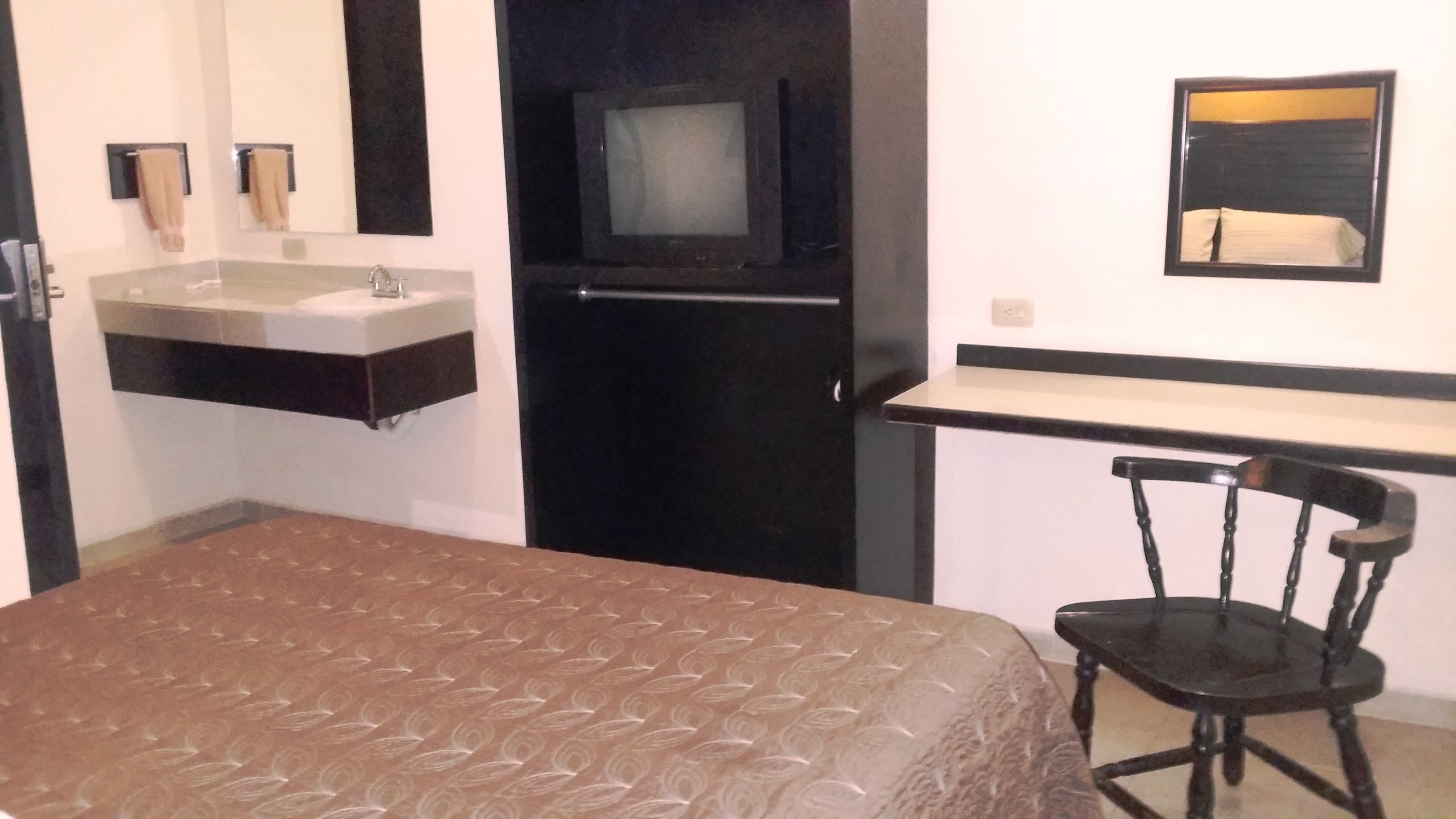 A bedroom with a bed, a chair, a desk, a television, and a mirror.
