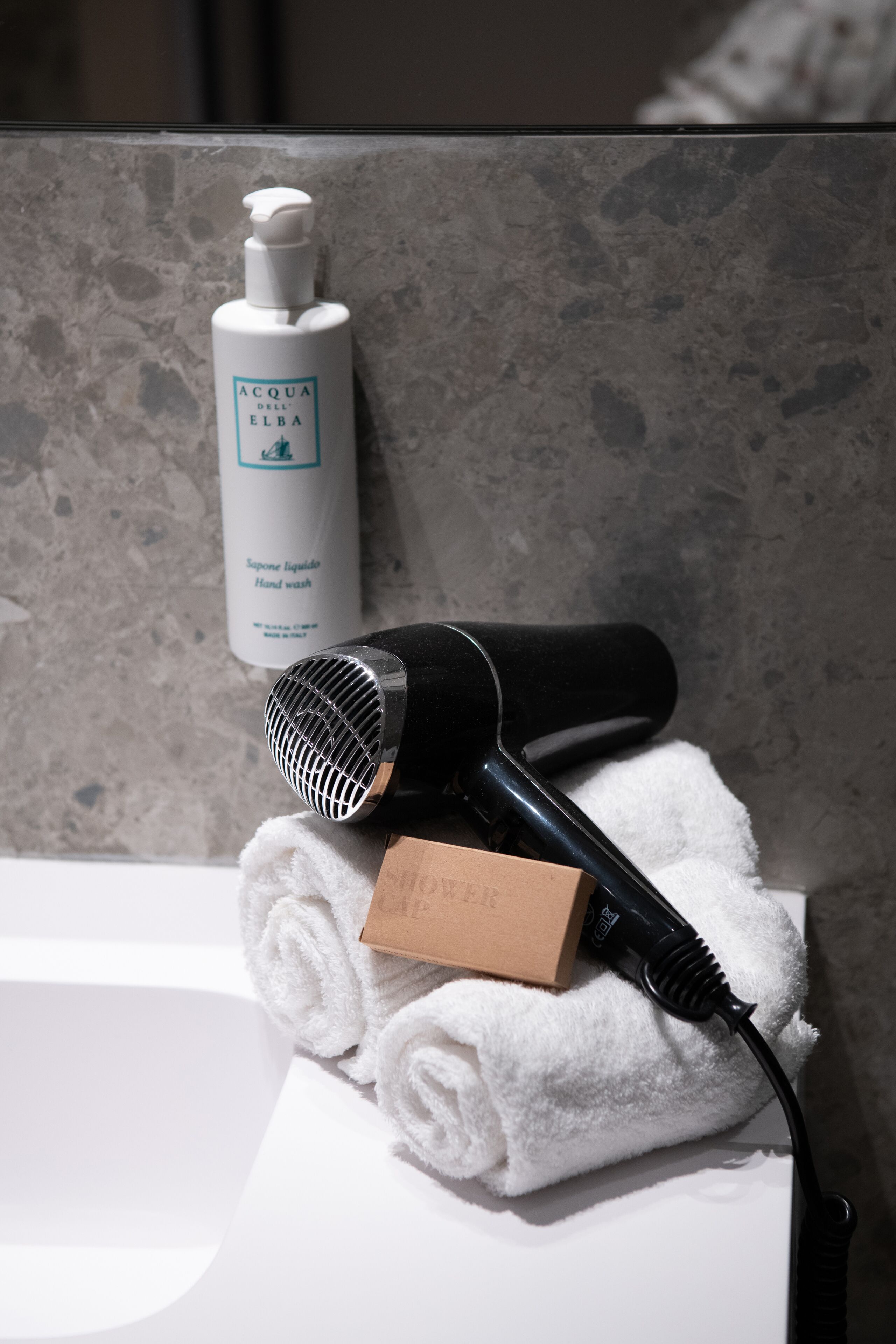 A bathroom with a white sink, a hairdryer, a towel, and a bottle of hand wash soap.